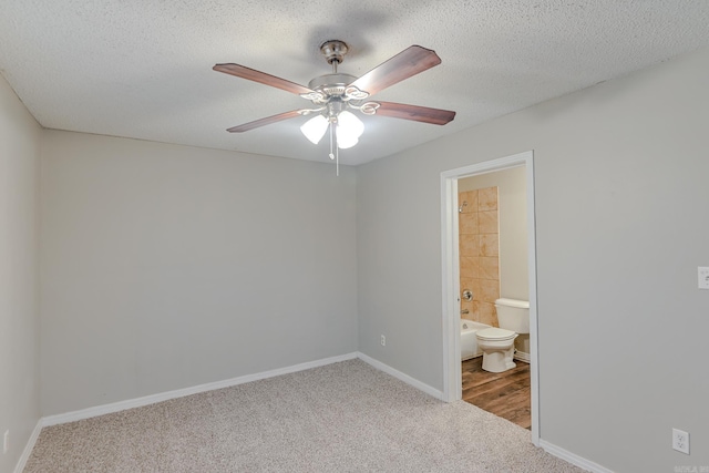 unfurnished bedroom featuring carpet flooring, a textured ceiling, ensuite bath, and ceiling fan