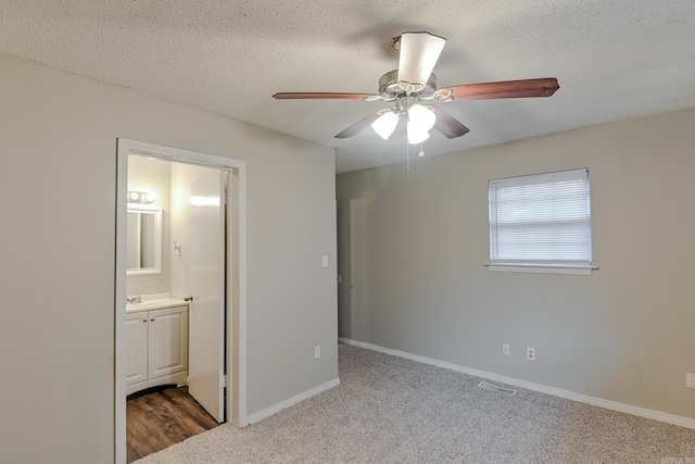 unfurnished bedroom with carpet, ensuite bathroom, ceiling fan, and a textured ceiling