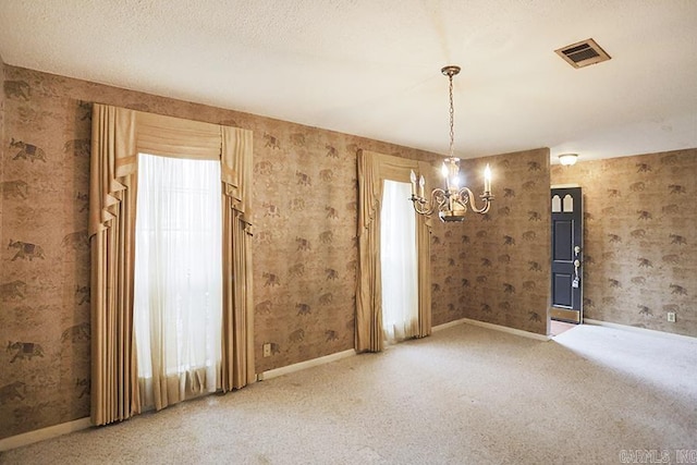 unfurnished room featuring a wealth of natural light, carpet, a textured ceiling, and an inviting chandelier