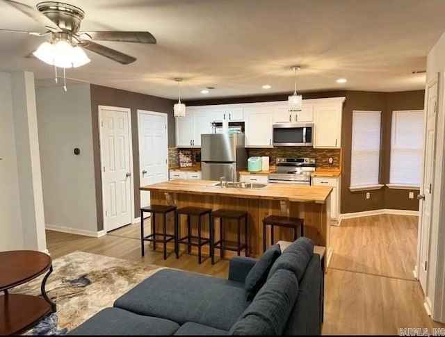 kitchen with hanging light fixtures, butcher block countertops, an island with sink, white cabinets, and appliances with stainless steel finishes