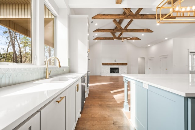 kitchen featuring sink, beamed ceiling, decorative light fixtures, hardwood / wood-style flooring, and a fireplace