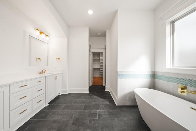 bathroom with vanity, a healthy amount of sunlight, a bath, and tile walls