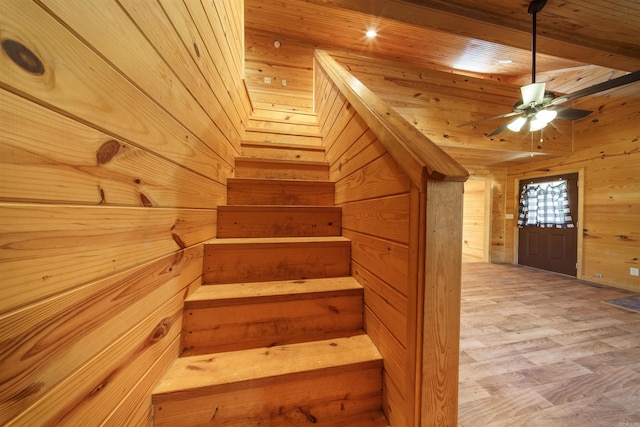 stairs with wooden walls, beamed ceiling, ceiling fan, and hardwood / wood-style flooring