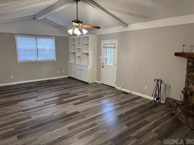 unfurnished living room with a textured ceiling, dark hardwood / wood-style floors, a stone fireplace, and ceiling fan