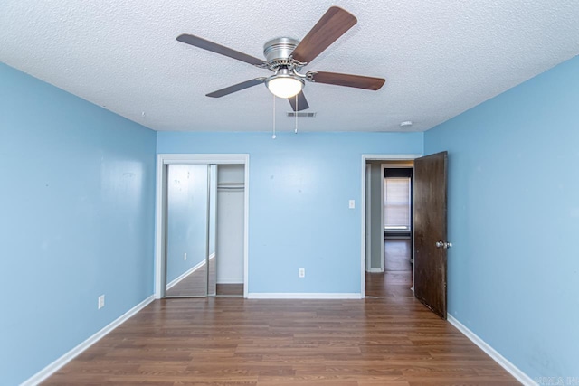 unfurnished bedroom with a textured ceiling, ceiling fan, dark wood-type flooring, and a closet