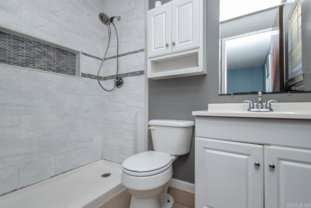 bathroom with tile patterned flooring, vanity, toilet, and tiled shower