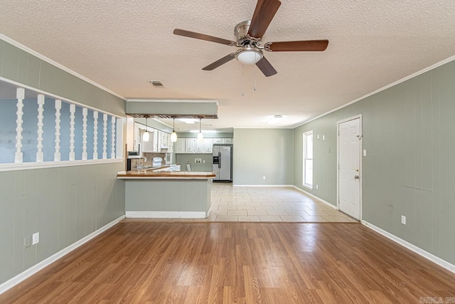 unfurnished living room featuring crown molding, wooden walls, ceiling fan, light wood-type flooring, and a textured ceiling