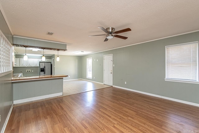 unfurnished living room with ceiling fan, ornamental molding, a textured ceiling, and light hardwood / wood-style flooring