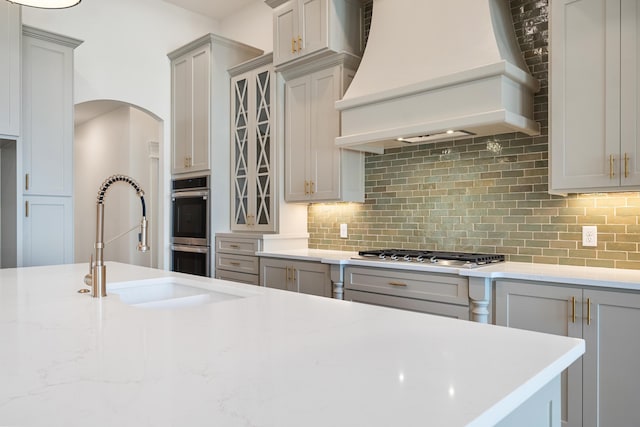 kitchen featuring sink, gray cabinetry, custom range hood, stainless steel appliances, and backsplash