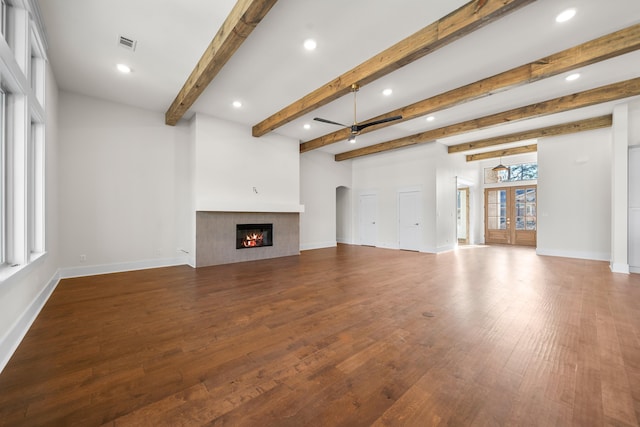 unfurnished living room featuring hardwood / wood-style flooring, beam ceiling, a tiled fireplace, and french doors