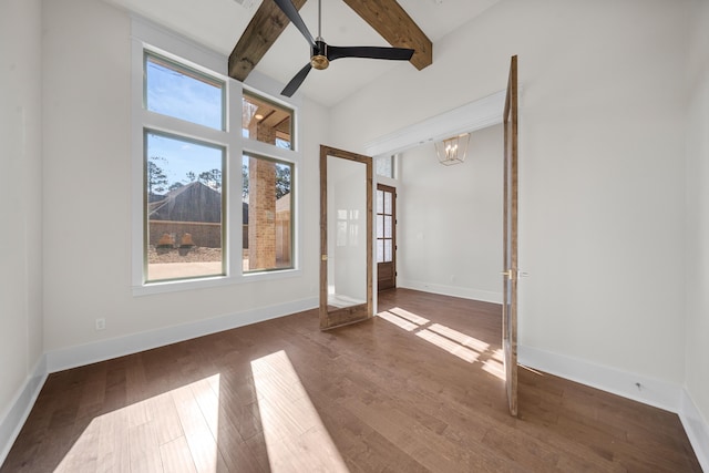 spare room featuring dark wood-type flooring, ceiling fan with notable chandelier, beam ceiling, and a towering ceiling