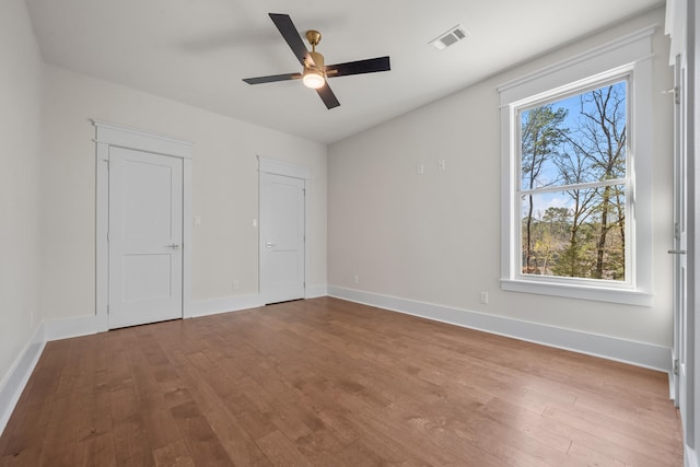 unfurnished bedroom featuring multiple windows, hardwood / wood-style flooring, and ceiling fan