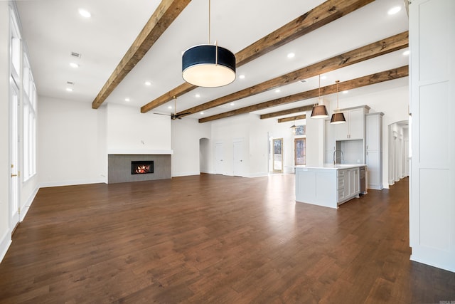 unfurnished living room with beamed ceiling, ceiling fan, dark hardwood / wood-style floors, and sink