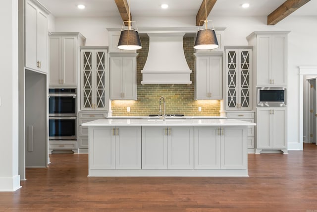 kitchen with hanging light fixtures, appliances with stainless steel finishes, an island with sink, and premium range hood