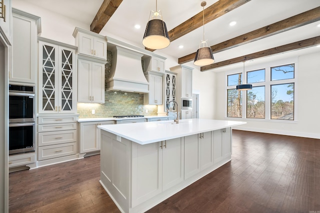 kitchen featuring a center island with sink, custom range hood, pendant lighting, stainless steel appliances, and backsplash