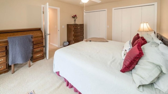 bedroom with ceiling fan, light carpet, and two closets