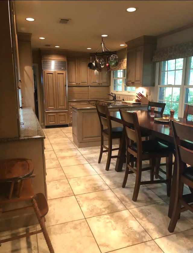 kitchen featuring a kitchen island, dark stone counters, pendant lighting, a breakfast bar, and light tile patterned floors