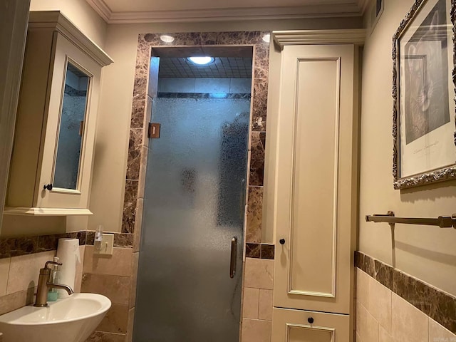 bathroom featuring tile walls, a shower with door, ornamental molding, and sink