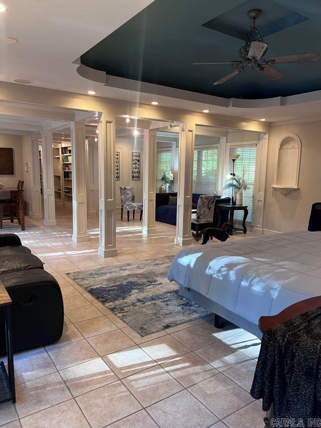 bedroom featuring light tile patterned floors, a tray ceiling, ceiling fan, and decorative columns