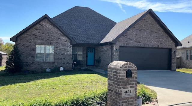 view of front facade featuring driveway, brick siding, a shingled roof, an attached garage, and a front yard