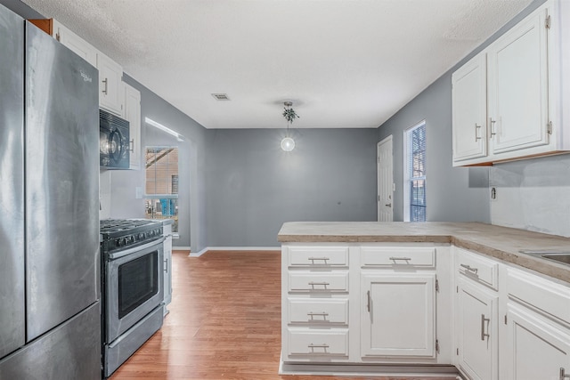 kitchen with kitchen peninsula, light hardwood / wood-style flooring, appliances with stainless steel finishes, decorative light fixtures, and white cabinetry