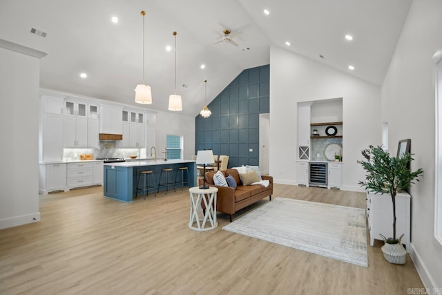 living room featuring ceiling fan, sink, light hardwood / wood-style flooring, high vaulted ceiling, and wine cooler