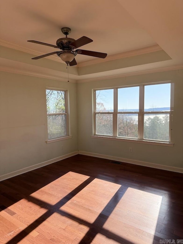 empty room with ceiling fan, ornamental molding, dark wood-type flooring, and a tray ceiling