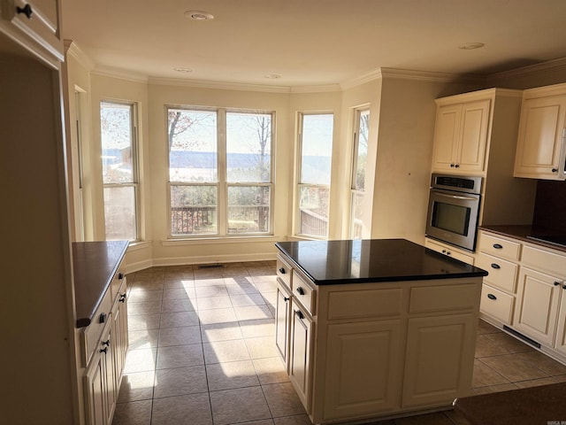 kitchen featuring stainless steel oven, a kitchen island, ornamental molding, and light tile patterned floors