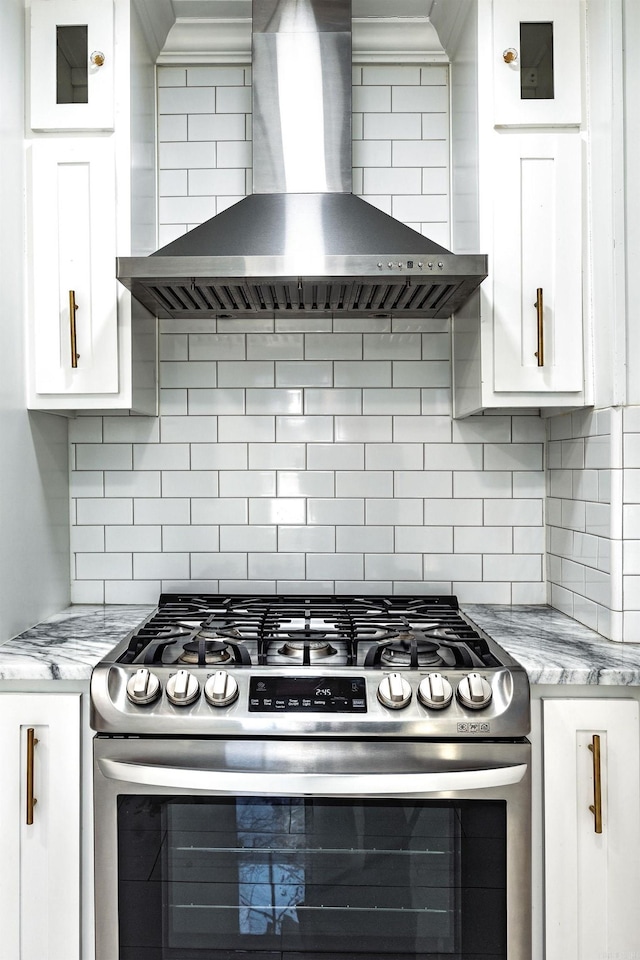 kitchen featuring light stone counters, white cabinets, wall chimney range hood, and stainless steel gas range