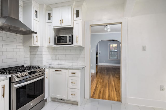 kitchen with white cabinets, light stone counters, wall chimney exhaust hood, and appliances with stainless steel finishes