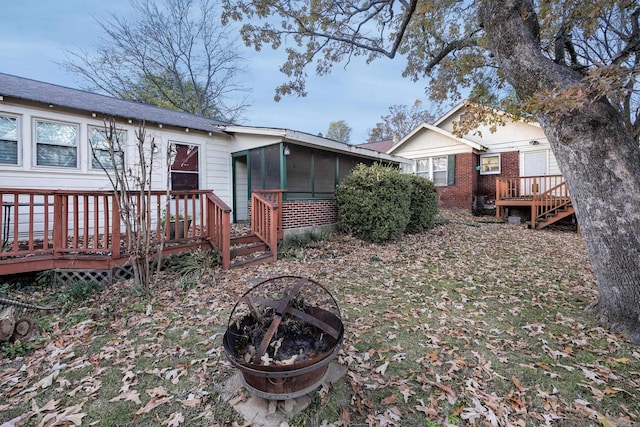 rear view of property with a fire pit, a deck, and a sunroom