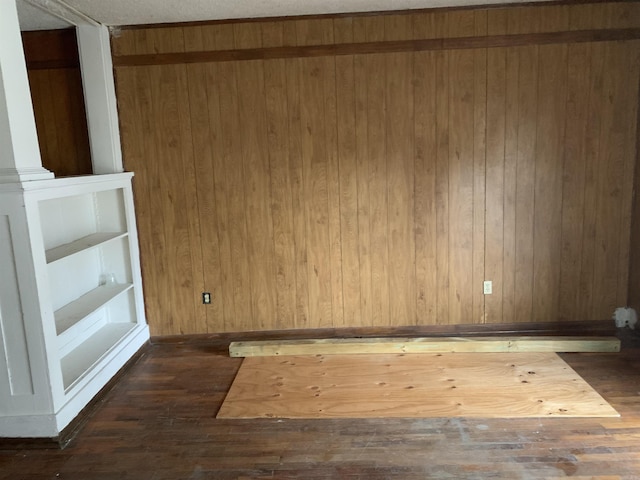 empty room featuring wooden walls, dark wood-type flooring, and a textured ceiling