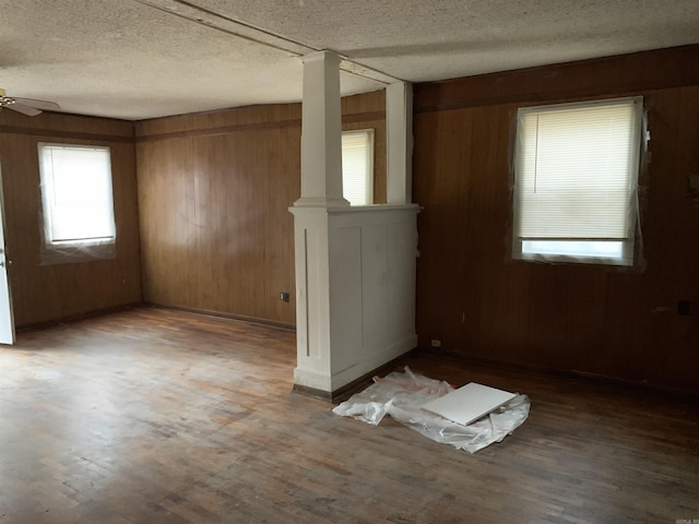 unfurnished room with a textured ceiling, wooden walls, ceiling fan, and dark hardwood / wood-style floors