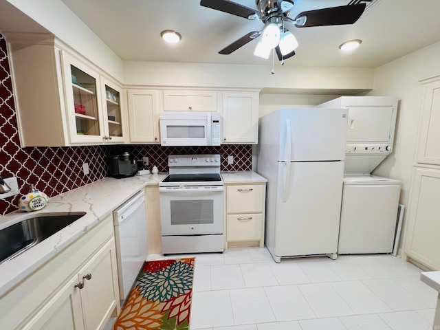 kitchen with white appliances, sink, decorative backsplash, stacked washing maching and dryer, and light stone countertops