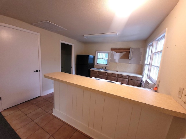 kitchen with plenty of natural light, black fridge, kitchen peninsula, and light tile patterned flooring