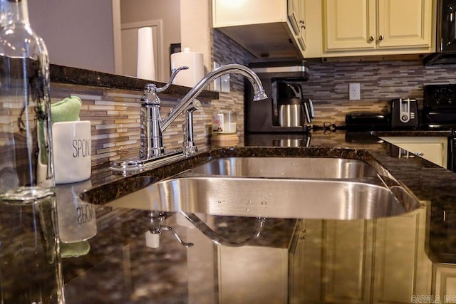 kitchen featuring tasteful backsplash, dark stone countertops, stove, and sink