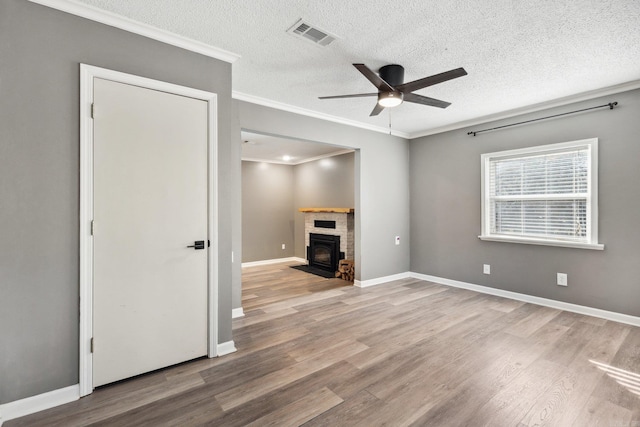 unfurnished living room with hardwood / wood-style flooring, ceiling fan, a wood stove, and crown molding