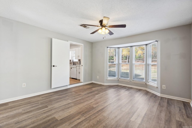 unfurnished room featuring a textured ceiling, ceiling fan, wood-type flooring, and sink