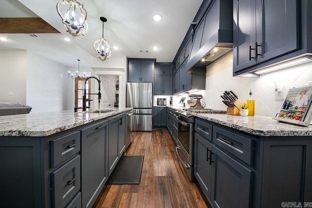 kitchen with stainless steel appliances, a kitchen island with sink, dark wood-type flooring, wall chimney range hood, and hanging light fixtures