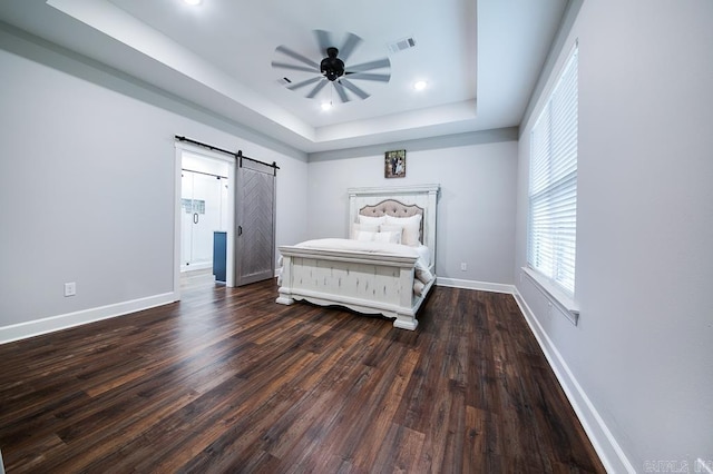 bedroom with a tray ceiling, a barn door, ceiling fan, and dark wood-type flooring