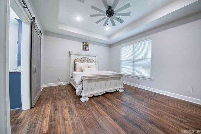 bedroom featuring dark hardwood / wood-style flooring, a barn door, a raised ceiling, and ceiling fan