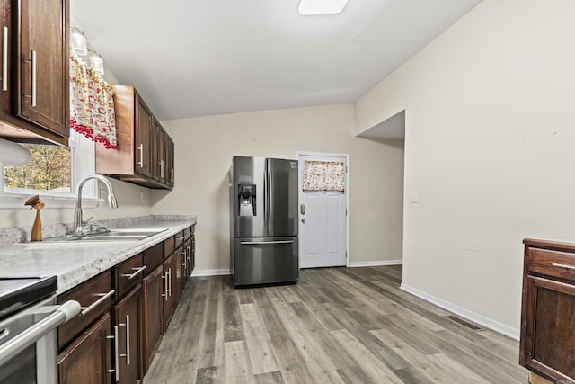 kitchen with lofted ceiling, sink, light hardwood / wood-style flooring, stainless steel fridge, and dark brown cabinetry