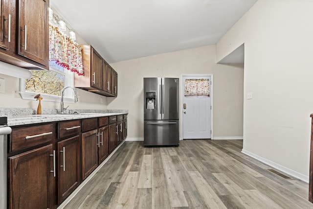 kitchen with light stone counters, dark brown cabinets, vaulted ceiling, light hardwood / wood-style flooring, and stainless steel fridge with ice dispenser