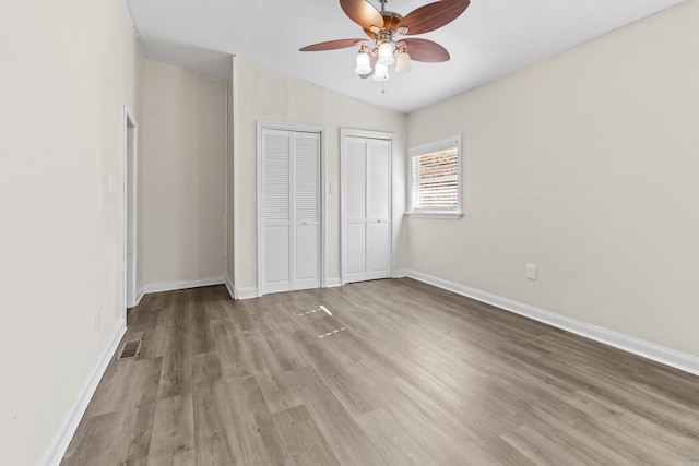 unfurnished bedroom featuring ceiling fan, multiple closets, light hardwood / wood-style flooring, and vaulted ceiling