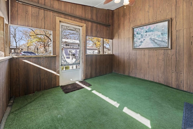 empty room with ceiling fan, wood walls, and dark colored carpet