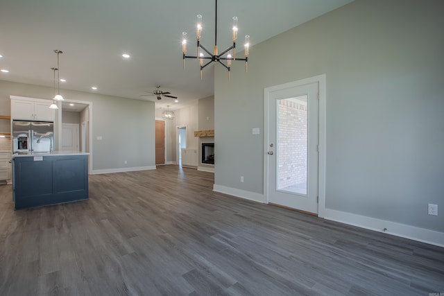 unfurnished living room with dark wood-type flooring and ceiling fan with notable chandelier