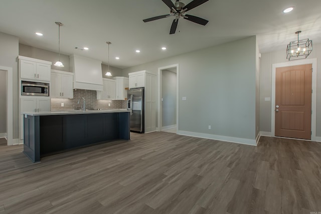 kitchen featuring appliances with stainless steel finishes, a kitchen island with sink, white cabinets, hardwood / wood-style floors, and hanging light fixtures