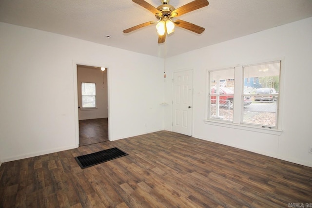 empty room with a textured ceiling, a wealth of natural light, ceiling fan, and dark hardwood / wood-style floors