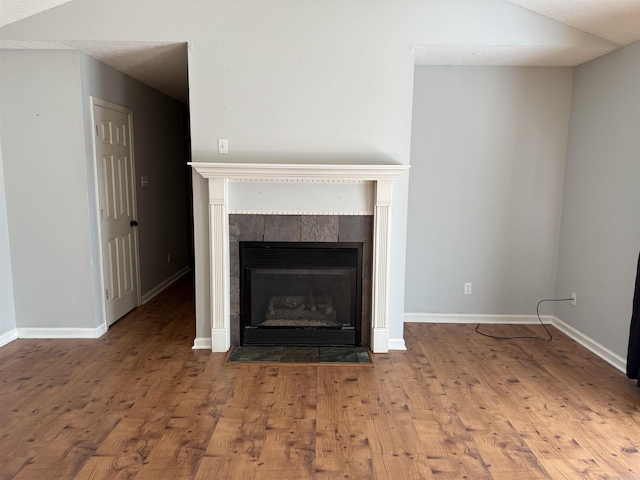 unfurnished living room with a tile fireplace, hardwood / wood-style flooring, and lofted ceiling