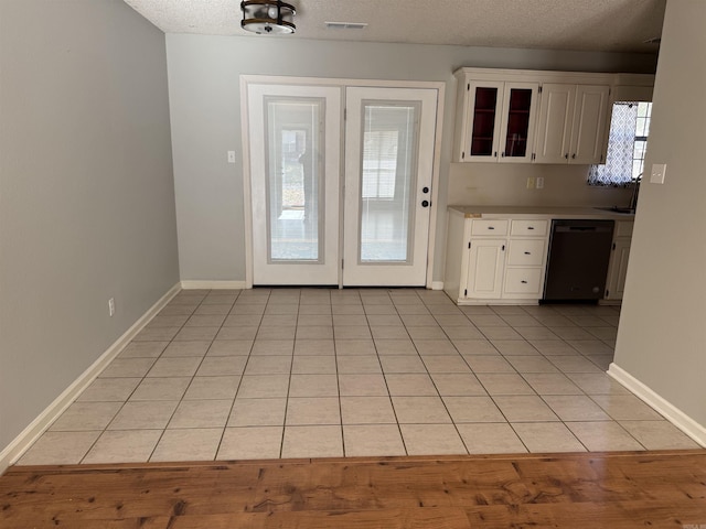 kitchen featuring white cabinets, light tile patterned floors, black dishwasher, and a textured ceiling